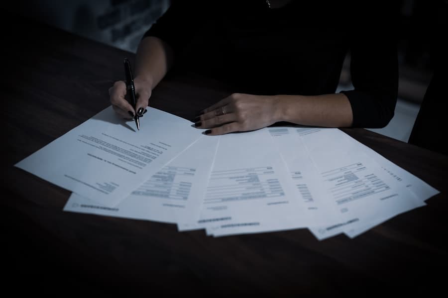 Persona firmando un abanico de papeles administrativos sobre una mesa oscura
